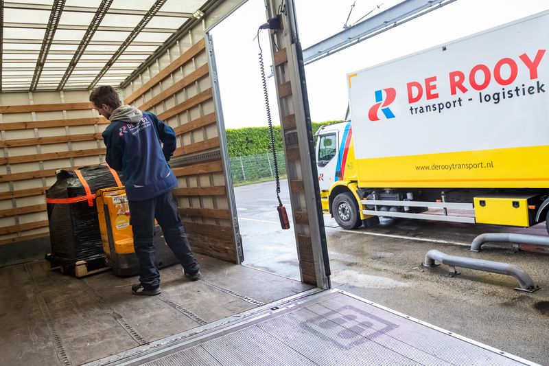 Medewerker laadt pallets in een bakwagen, op de achtergrond een vrachtwagen van De Rooy Transport